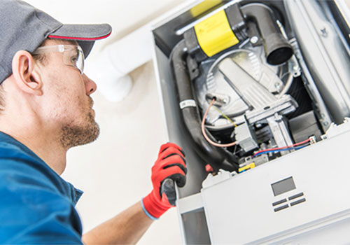 HVAC technician troubleshooting a gas furnace with the access panel open during a repair