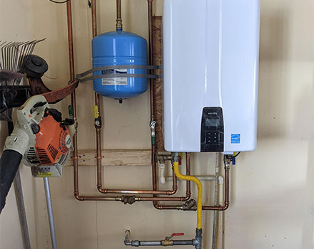 Wall-mounted tankless water heater with blue expansion tank and copper piping repaired by Aire One East in Durham Region