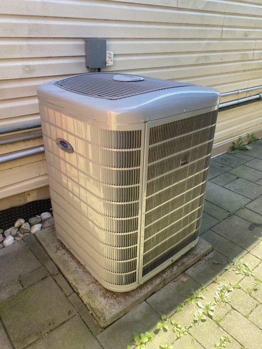 Carrier air conditioner condenser unit installed on a patio stone beside a home