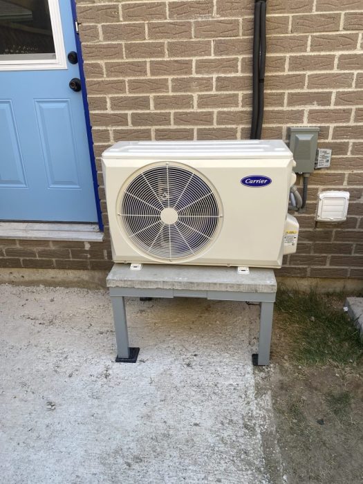 Carrier ductless mini-split outdoor unit mounted on a stand beside a side door