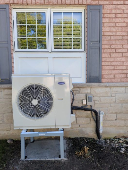 Carrier heat pump outdoor unit installed on a stand below a window