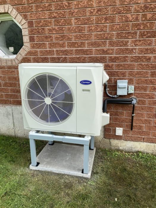 Carrier heat pump outdoor unit installed on a raised stand against a brick wall